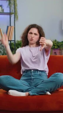 Hoşlanmamak. Mutsuz kadın işaret hareketi gösteriyor, hoşnutsuzluğunu dile getiriyor, hoşnutsuzluğunu dile getiriyor, modern ev dairelerinde kötü işler yapıyor. Oturma odasında kanepede hoşnutsuz bir kız. Dikey çekim