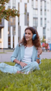 Kablosuz kulaklıklı, neşeli, çocukluk çağındaki çocuk dışarıda dans ederken en sevilen disko rock 'n roll müziğini dinliyor. Şehir parkında çimlerde oturan kız
