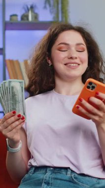 Aile bütçesi planlamak. Gülümseyen genç bir kadın nakit para sayıyor, akıllı telefon kullanıyor ev faturalarını hesaplıyor. Gelirinden tatmin olan ve planlı tatil ve hediyeler için para biriktiren bir kız. Dikey