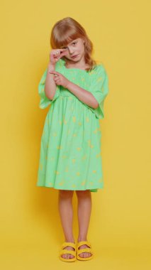 Biraz daha, lütfen bana ver. Sarışın çocuk, küçük bir jest yapıyor. Şüpheci bir gülümsemeyle minimum işaret veriyor. Boyut olarak küçük. Sarı arka planda küçük çocuklar. Dikey