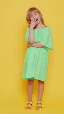 Bıkkın sarışın kız çocuğu esniyor, uykulu, ilgisiz, uykusuz tembel, eğitimden sonra uykusuzluk çekmekten sıkılmış. Sarı arka planda izole edilmiş küçük çocuklar. Dikey