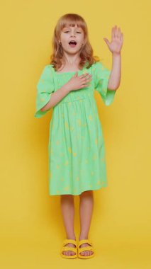 Dürüst olacağıma yemin ederim. Samimi sorumluluk sahibi kız çocuğu yemin etmek için elini kaldırıyor, dürüst olacağına söz veriyor kibar olup elini göğsüne koyuyor. Sarı arka planda küçük çocuklar. Dikey