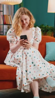 Kanepede oturan kızıl saçlı genç kadın, cep telefonu kullanıyor ve gülümsüyor. İnternet üzerinden akıllı telefon sosyal medya uygulamaları üzerinden rahatlama filmi izlerken mesajlaşan bir kız. Dikey