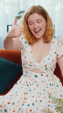 Gibi. Mutlu, heyecanlı kızıl saçlı kadın onaylayıcı bir şekilde kameraya bakıyor olumlu bir şey işaret ediyor, iyi haber, olumlu geri bildirim gibi. Sınıftaki kanepede oturan genç kız. Dikey