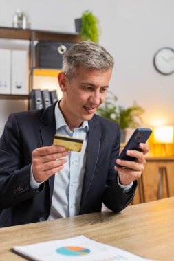 Para transfer ederken banka kartı ve akıllı telefon kullanan, internet üzerinden alışveriş yapan, merkez ofisteki masada oturan Kafkasyalı genç bir serbest çalışan. Uzaktan kumanda işinde çalışan gülümseyen yakışıklı adam..