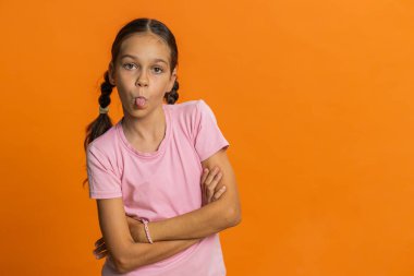 Neşeli, komik, genç liseli kız kameraya dil gösteriyor, dalga geçiyor, şakalaşıyor, zorbalıkla dalga geçiyor. Turuncu arka planda 10 yaşında çocuk.