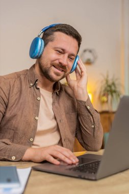 Memnuniyetle ofis masasında oturmuş, kablosuz kulaklıkla en sevilen enerjik müziği dinleyen iş adamı. Mutlu serbest çalışan adam dinleniyor, masadaki dizüstü bilgisayarla mola veriyor..