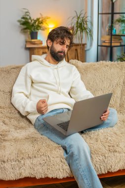 Evdeki kanepede oturan üzgün genç Hintli adam dizüstü bilgisayar kullanıyor ve stres altında. Sakallı adam kayıplara tepki veriyor. Oturma odasındaki internet sitesinde kötü haberler. Bilgisayar virüsü.