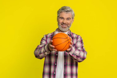 Olgun bir erkek, basketbolu ustalıkla elinde zıplatır, oyun oynar, kendine güvenini gösterir, kontrollü davranır. Sarı arka plandaki orta yaşlı adam atletik inceliği, parmak ucunda dönen topu gösteriyor.