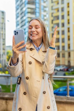 Cep telefonu kullanan Kafkas iş kadınının şehir merkezindeki akıllı telefon bahsini kazanan kadını şaşırtarak zafer başarısını kutlamasına şaşırdım. Şehir sokağında duran kız.