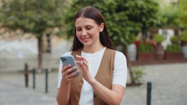Akıllı telefon kullanarak gülümseyen genç bir kadın. Kısa mesajlar yazarak interneti tarıyor, işi bitiriyor, dışarıdaki kameralara bakıyor. Şehir caddesinde duran kız turist. Kasaba yaşam tarzları