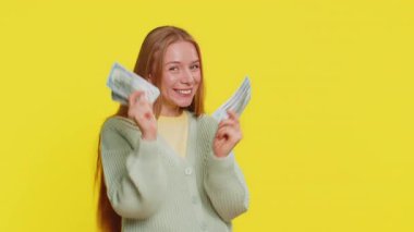 Zengin, mutlu, orta yaşlı, dans eden beyaz bir kadın elinde dolar banknotlarıyla hayranı, başarılı bir iş piyangosunun kazananı gibi para sallıyor. Sarı arkaplanda izole edilmiş kız