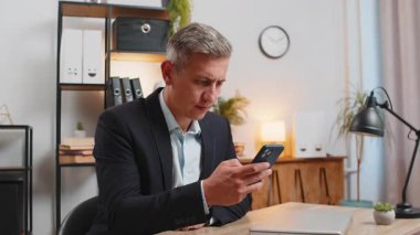 Üzgün genç işadamı, ofis masasında akıllı telefondan kötü haberler okuyor. Resmi takım elbiseli üzgün erkek işveren hoş olmayan tebligattan rahatsız, internetteki bilgiden şok olmuş, mesajla depresyona girmiş..