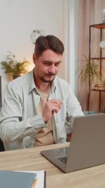 Oturma odasındaki işi bitirdikten sonra masadaki bilgisayarı kapatan genç adam. Happy Kafkasyalı serbest çalışan adam ev masasında uzaktan kumandayla çalışıyor. E-öğrenme, internette gezinme. Dikey