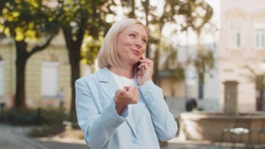 Gülümseyen, kendine güvenen, beyaz, takım elbiseli kadın iş kadını hoş bir iş görüşmesi yapan, cep telefonuyla konuşan, akıllı telefon bağlantısı olan şehir caddesinde duran....