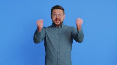 Mutlu beyaz adam başarıyı kutluyor zaferi, doğum gününü, piyango hedefini başarıyı iyi haber zaferini. Genç yakışıklı adam mavi stüdyo geçmişinde izole edilmiş.