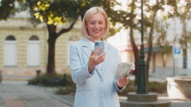 Beyaz, olgun bir iş kadını, şehir caddesinde duruyor. Elinde cep telefonuyla, nakit parayla bahis oynayarak kazandığını gösteriyor. Açık havada takım elbiseli orta yaşlı bir kadın akıllı telefonlu ve bir sürü parası var..