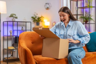 Evdeki kanepede oturan mutlu beyaz kadın paketleri açıyor. İnternetten alışveriş yapan kız müşteri, karton kutu açıyor ve hızlı posta yoluyla oda dairesinden hediye alıyor..