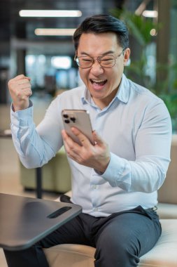 Akıllı telefon üzerinde çalışan mutlu, şaşkın genç işadamı piyango kazanan bir galibiyet oyunuyla şok oldu. Kariyer başarısı iyi haber. Ofis otel lobisinde oturan gömlekli, heyecanlı, olgun bir adam..