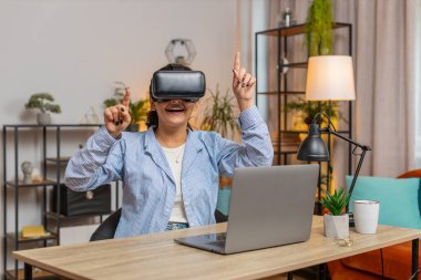 Evde ofis masasında otururken VR kulaklığı test eden Hintli serbest çalışan sürpriz bir kadın. Evde uzaktan kumanda ile çalışan genç işadamı kız sunum yapıyor. Yaşam biçimi.