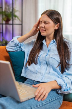 Dizüstü bilgisayar kullanan yorgun genç bir kadın, baş ağrısı, tansiyon ve migren sorunu, evde stres. İnternette çalışan, mesaj yollayan, online alışveriş yapan, film izleyen bir kız. Yaşam Tarzları.