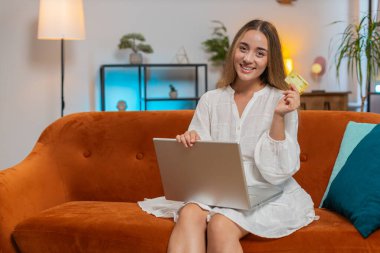 Güzel beyaz kadın kredi kartı tutuyor ve dizüstü bilgisayar kullanıyor. Çevrimiçi dükkanlarda numaralarını yazan, internetten ödeme yapan genç bir kadın. Başarılı bir alışverişle mutlu bir şekilde gülümsüyor. Para harcamak konsepti. Yaşam biçimi
