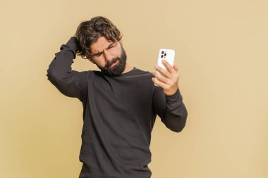 Lübnanlı genç adam cep telefonu daktilo yazarken, şaşırarak aniden piyango sonuçlarını kaybediyor, kötü talih, kayıp, başarısızlık. Yakışıklı Hintli erkek, bej renkli stüdyo arka planında izole edilmiş..