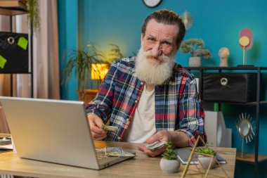 Kafkasyalı kıdemli adam nakit para sayıyor ve ofisteki bilgisayarı kullanıyor. Başarılı serbest çalışan büyükbaba makama yığınla para getiriyor kar paylarını hesaplıyor maaş gelirlerini finanse ediyor