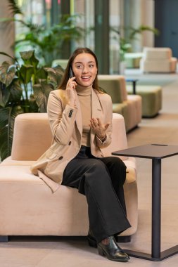 Telefon, iyi haber, dedikodu. Kafkasyalı genç iş kadını mutlu bir sürpriz. Akıllı telefondan hoş sohbetler ediyor. Modern ofis lobisinde arkadaşıyla eğleniyor. Otel odasında oturan bayan.