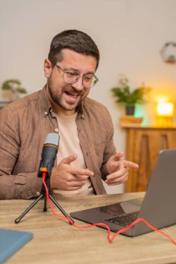Mutlu heyecanlı blogger adam podcast yapıyor, atölye veriyor, webinar yapıyor. Genç Kafkasyalı nüfuzlu adam mikrofon ve dizüstü bilgisayara konuşuyor, video görüşmesi yapıyor, merkez ofiste tartışıyor..