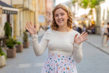 Hoş geldiniz. Kızıl saçlı genç bayan kameraya arkadaşça gülümsüyor, iki elini sallayarak selam veriyor ya da dışarıda misafirperver bir şekilde karşılıyor. Şehir caddesinde yürüyen bir kız. Şehir dışında.