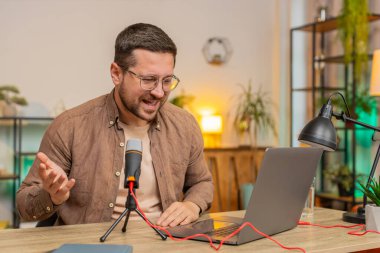 Mutlu heyecanlı blogger adam podcast yapıyor, atölye veriyor, webinar yapıyor. Genç Kafkasyalı nüfuzlu adam mikrofon ve dizüstü bilgisayara konuşuyor, video görüşmesi yapıyor, merkez ofiste tartışıyor..