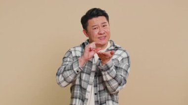 Biraz daha, lütfen bana ver. Asyalı orta yaşlı bir adam şüpheci bir gülümseme ile küçük boylarda ve yalvaran bir gülümseme gösteriyor. Bej arka planda olgun Çinli bir adam.