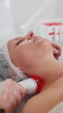 Güzellik uzmanı, kadına yüz ve boyun kaldırma prosedürü yaptırıyor. Kolajen maskesi. Kozmetik uzmanı vakum yüz masajı terapisi için elektrikli ekipman kullanıyor. Cilt bakımı, güzellik tedavisi. Dikey çekim