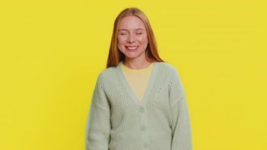 Kameraya gülümseyen beyaz bir kadın, el sallayarak selam veriyor ya da davetkar bir yüz ifadesiyle veda ediyor. Sarı stüdyo arka planında izole güzel bir kız.