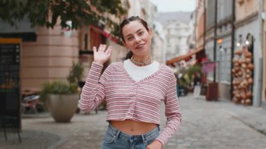 Hoş geldiniz. Diş teli takmış genç, mutlu bir kadın kameraya gülümseyen, el sallayan, el sallayan, ya da misafirperver bir yüz ifadesiyle veda eden. Şehir caddesinde duran kız
