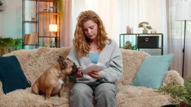 Beyaz saçlı genç bir kadın evdeki kanepede stres belirtileri gösterirken faturaları ciddi bir şekilde kontrol ediyor. Pug dog sakince onun yanına uzanır, duygusal rahatsızlığı hisseder ve ona huzur teklif eder..