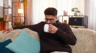 Evdeki Hintli adam kanepede oturur ve uzun bir günün ardından gülümseyen çay ya da kahvenin tadını çıkarır. Arap adam aroma soluyor ve huzurlu bir ruh hali ve huzur dolu bir an yaşıyor..