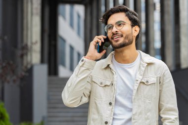 Uzaktan iletişim kuran mutlu Hintli adam dışarıda akıllı telefonla konuşuyor. Arap Hindu adam şehir merkezinde beklenmedik bir şekilde dedikodu yapıyor. İş adamları