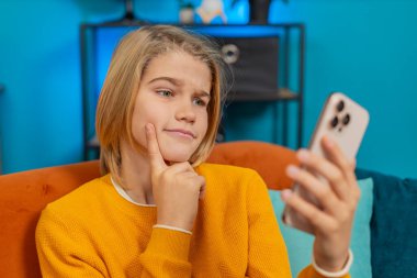 Beyaz çocuk evde akıllı telefondan bulmaca çözme girişiminde bulunuyor. Düşünceli ifade çözüm bulma seviyesini yükseltiyor, koltukta oturup memnuniyet gösteriyor.