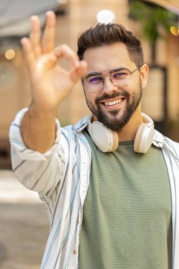 Gülümseyen genç milenyum çocuğunun el işaretini gösteren bir portresi. Beyaz tenli yakışıklı adam her şeyi gösteriyor. Güzel vücut dili. Gözlüklü turist kameraya gülümsüyor..