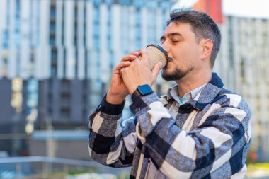 Mutlu Kafkasyalı olgun bir adam sabah kahvesinin tadını çıkarıyor sıcak içecek ve dışarıda gülümsüyor. Dinleniyorum, ara veriyorum. Şehir merkezindeki caddede dikilen ve kahve içen adam. Kasaba yaşam tarzları.