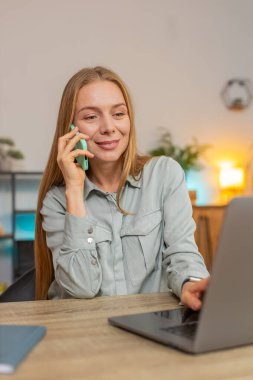 Olgun bir iş kadını cep telefonu ve dizüstü bilgisayar kullanarak müşteriye cevap veriyor. Sohbet. Uzaktan kumandayla çalışan beyaz bir kadın ofis masasında konuşuyor..