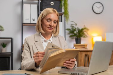 Kafkasyalı orta yaşlı iş kadını ilginç kitaplar okuyor, sayfalarca gülümsüyor işten sonra edebiyattan zevk alıyor. Bilgisayarlı serbest çalışan mutlu bayan ev ofisinde dinleniyor.
