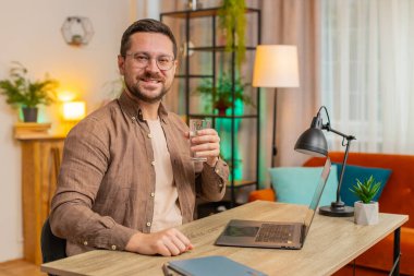 Ofis odasında dizüstü bilgisayarla çalışırken masa başında oturmuş su içen Kafkasyalı bir iş adamı. Genç erkek serbest çalışan adam bilgisayar ekranı internette geziniyor..