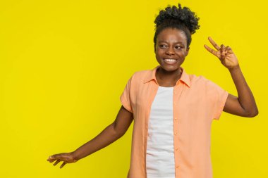 Afrika kökenli Amerikalı bir kadın komik el hareketleriyle dans ediyor, neşe ve neşe saçıyor. Sarı arka planda müzik dinleyen, neşeli ritim ve kaygısız tavır sergileyen siyah bir kız.