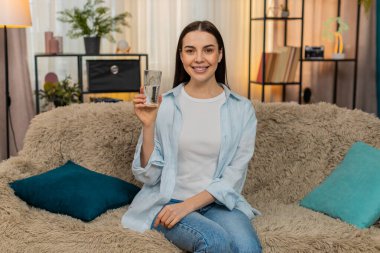 Sıcak havadan sonra susamış genç bir kadın saf filtrelenmiş su içiyor. Kanepede oturan beyaz bir kız sağlıklı yaşam tarzını, susuzluğunu iyi alışkanlıklarını tatmin ve tazelenmiş duygusal duygularını destekliyor.