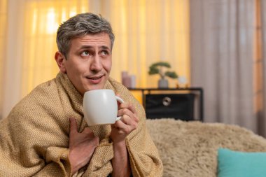 Evdeki üzgün genç adam bir fincan çayla battaniyeye sarılmış, hasta görünüyor ve öksürüyor. Kanepedeki beyaz adam soğuk algınlığı belirtileri gösteriyor, sessizce dinleniyor ve hafif bir hastalık ve yorgunluktan kurtulmaya çalışıyor.