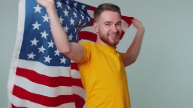 Tişörtlü, Amerikan bayrağına sarılı sakallı bir gencin portresi. Kutlama, insan hakları, özgürlükler. Bağımsızlık Günü. Stüdyoda çekilen yetişkin adam gri arka planda tek başına.