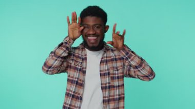 Komik, neşeli, 20 yaşında, tişörtlü, neşeli, suratını buruşturan, dil gösteren, neşeli, samimi bir yetişkin adam. Genç yakışıklı adam mavi duvarda tek başına.